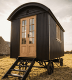 Portable shepherd's hut with wooden door and wheels in a field