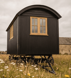 Black shepherd's hut with wooden windows in a field
