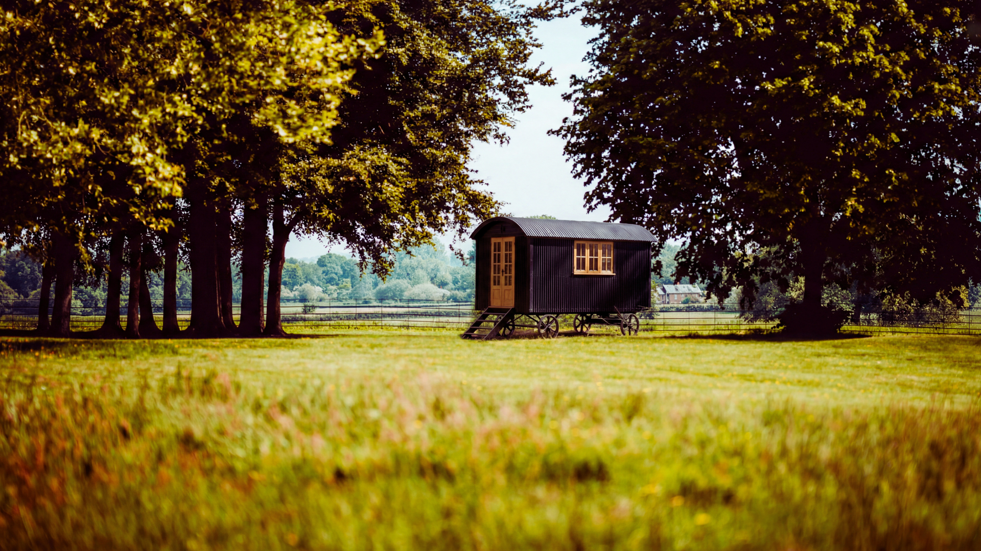 Traditional black corrugated shepherd hut with oak doors in a garden setting.