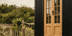 Close up of a traditional black corrugated shepherd hut with oak doors in a garden setting